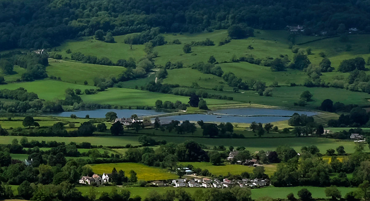 Rolling green Gloucestershire valley in the Cotswolds with hedged fields, a lake and scattered farmhouses